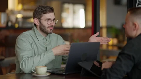 Engaging Conversation in a Cafe: Two Individuals Discuss Ideas While Sharing Stock Footage 344799984