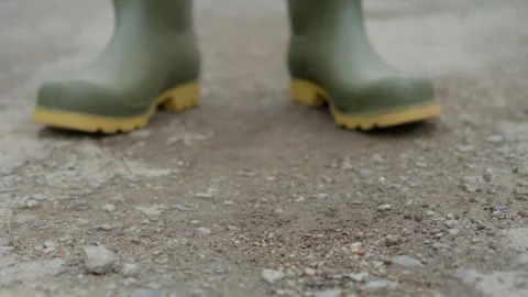 Engaging in gardening activities while wearing green boots on a gravel surface Stock Footage 309421780