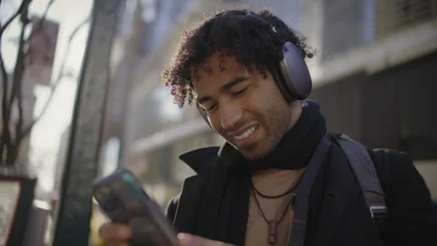 Engaging man on city street using mobile phone while enjoying music Stock Footage 312580985
