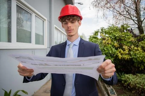 An engineer analyzes a floor plan while he is wearing a protective helmet. Stock Photos