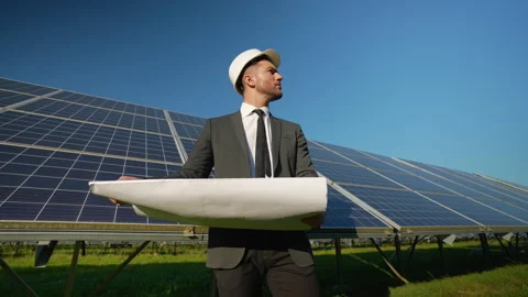 Engineer analyzing blueprints near solar panels in green field Stock Footage 296847891