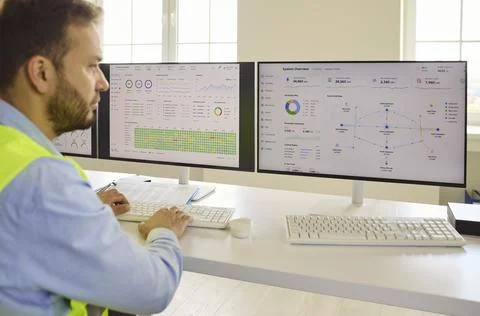 Engineer analyzing data on dual computer screens in industrial control room Foto stock