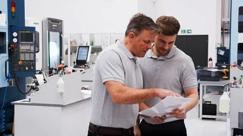 Engineer And Apprentice Discuss Plans On Floor Of Engineering Workshop Stock Footage 95508832
