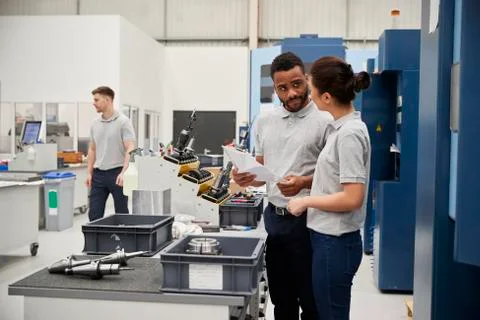 Engineer And Apprentice Meet On Floor Of Engineering Workshop 스톡 사진