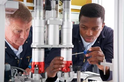 Engineer and apprentice working on machine in factory Stock Photos