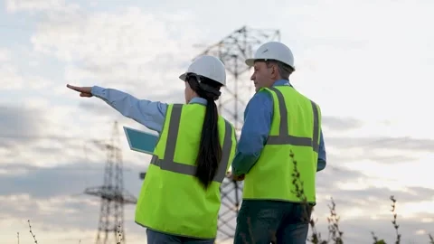 Engineer and safety inspector with tablet walk to power transmission lines Stock Footage 267575412