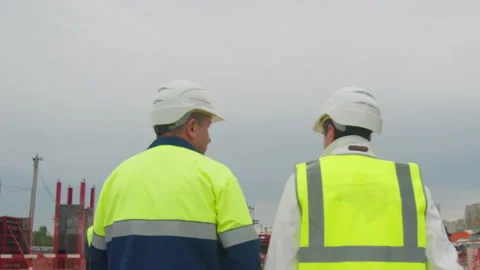 Engineer and taskmaster walk along construction site Stock Footage 200221073