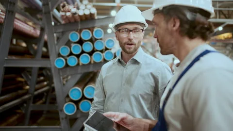 Engineer and Technician Talking Near Stacked Pipes in Industrial Warehouse Stock Footage 296265190