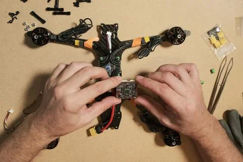 An engineer assembles a racing drone, carefully handling a flight controlle.. Stock Photos