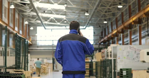 Engineer in in blue uniform is Walking Through Factory and talking on the mobile Stock Footage 91644721
