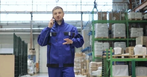 Engineer in in blue uniform is Walking Through Factory and talking on the mobile Stock Footage 91645592