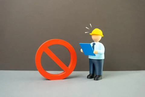 An engineer with blueprints surprised by a large prohibition symbol. Constr.. Stock Photos