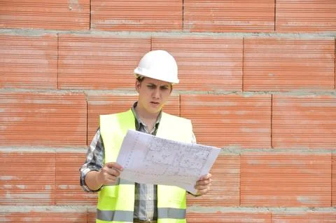 Engineer builder in front of orange brick wall with plan Stock-Fotos