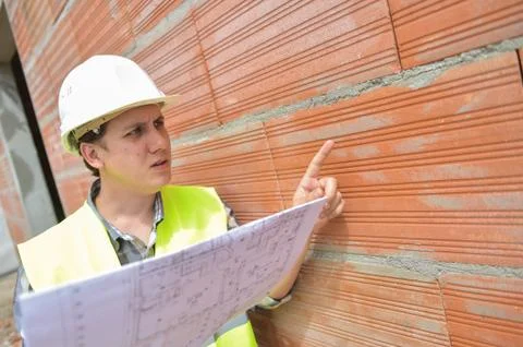 Engineer builder in front of orange brick wall with plan 스톡 사진