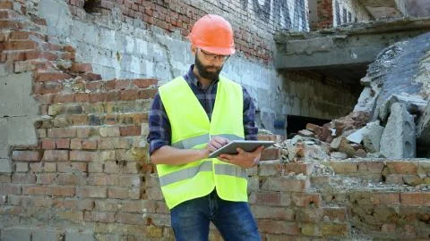 An engineer builder in a helmet is calculating the building demolition plan and Stock Photos