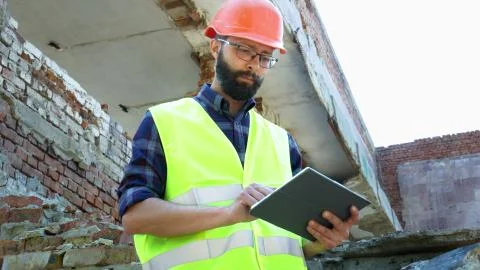 An engineer builder in a helmet use tablet, building demolition plan and looking Stock Photos