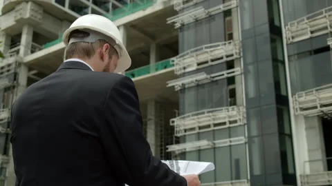 Engineer in business suit in white protective helmet works, stands with his back Stock Footage 171134448