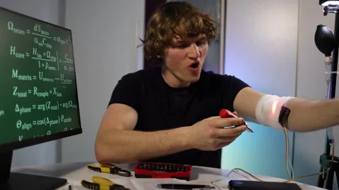 Engineer calibrates glowing arm implant while coding neural algorithms in home l Stockbeeldmateriaal 324443080