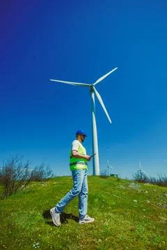 Engineer checks data on a device while walking near a wind turbine at a wind  Stock Photos