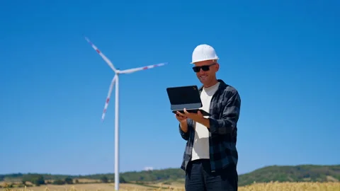 Engineer checks data in field near wind turbine under blue sky. A person uses a Stock Footage 342736897