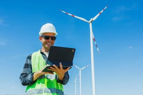 Engineer checks data on a laptop while standing at a wind farm on a clear d.. 스톡 사진