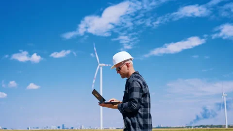 Engineer checks data on laptop in wind farm during day. A person stands in a Stock Footage 342737279