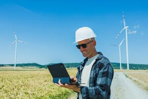 Engineer checks data on a tablet in a field with wind turbines nearby durin.. 스톡 사진
