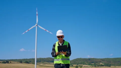 Engineer checks data at wind farm site during sunny day. A worker in a safety Stock Footage 342737583
