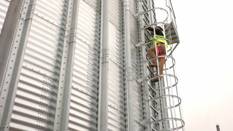 An engineer climbs a ladder on a silo to inspect the construction. Stock Footage 271629599