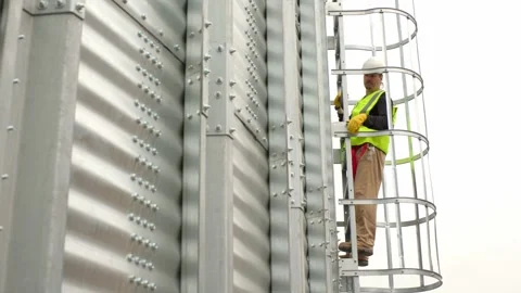 An engineer climbs a ladder on a silo to inspect the construction. Stock Footage 271629901