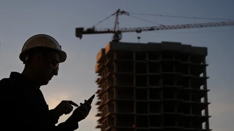 Engineer at the construction site using his phone texting something. Silhouette. Stockbeeldmateriaal 116784055