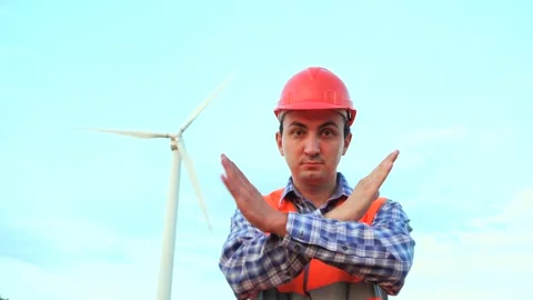 Engineer is crossing arms showing stop sign at wind turbine power plant on sky Stock Footage 137046483