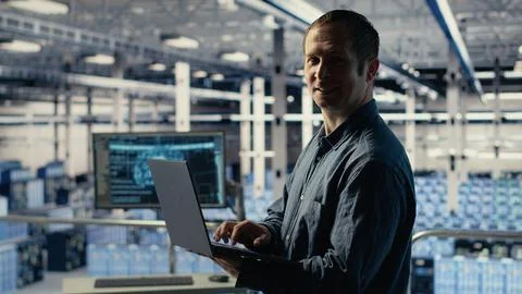 Engineer in data center checks AI dashboard using laptop during systems review 스톡 사진