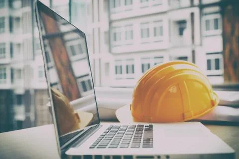 Engineer desk with laptop computer, orange helmet, blueprint roll Stock Photos