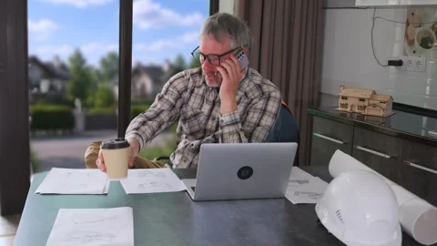 Engineer discussing construction project by phone while holding coffee at home Stock Footage 334870986