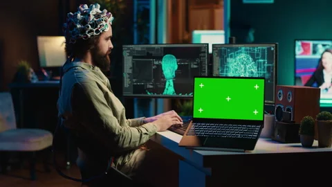 Engineer with EEG headset on merging with AI, green screen laptop Stock Footage 266951220