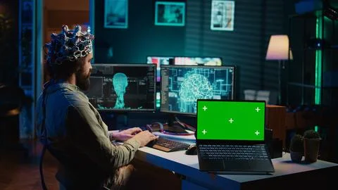 Engineer with EEG headset on merging with AI, green screen laptop Foto stock