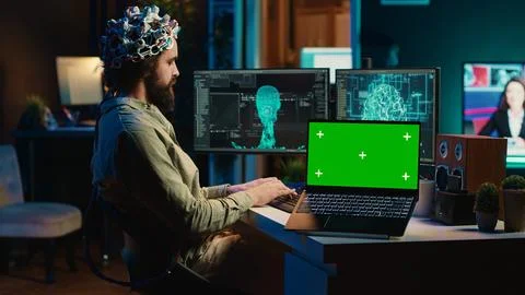 Engineer with EEG headset on merging with AI, green screen laptop Foto stock