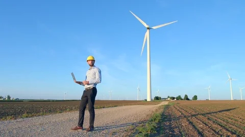 The engineer finishes work and leaves, looks at the windmills, holds a laptop in Stock-Footage 76576444