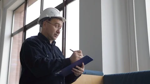 Engineer in glasses and a helmet writes information on work with a pen on paper Stock Footage 126576306