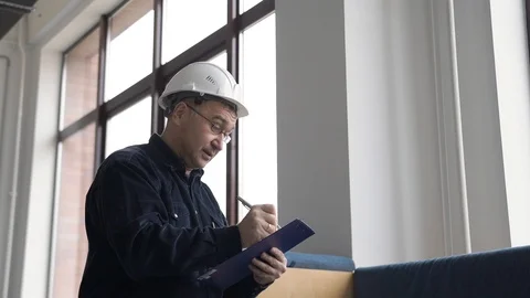 Engineer in glasses and a helmet writes information on work with a pen on paper Stock Footage 126576507