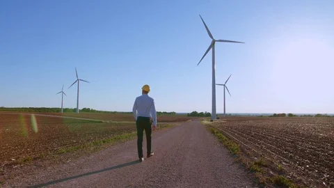 The engineer goes against the background of the windmills, stops and looks at 動画素材 76567893