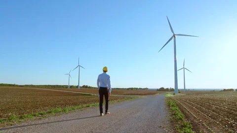 The engineer goes against the background of the windmills, stops and looks at Video stock 76591258