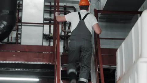 An engineer in a hard hat and uniform climbs a metal staircase at a factory. Stock Footage 306814738