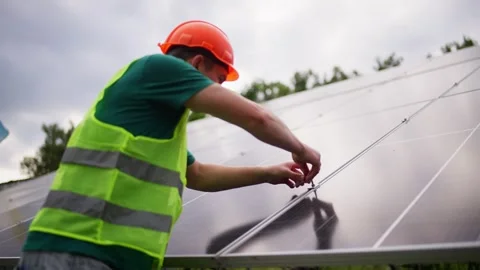 An engineer in a hard hat checks and tightens between solar panels. Stock Footage 319014510