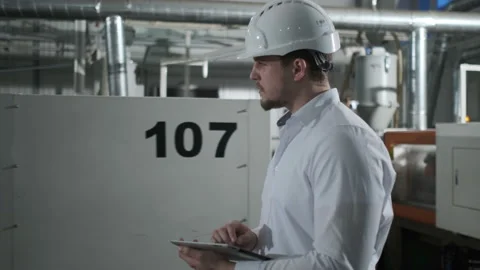 Engineer in hard hat is moving through a heavy industry factory with a tablet Stock Footage 114503465