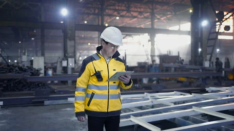 Engineer in hard hat is moving through a heavy industry factory with a tablet Stock Footage 237557414