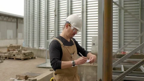 An engineer in a hard hat with a project in hand checks the construction status  Stock Footage 271629374