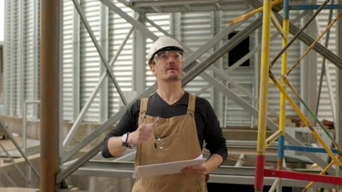 An engineer in a hard hat with a project in hand checks the construction status  Stock Footage 271629490