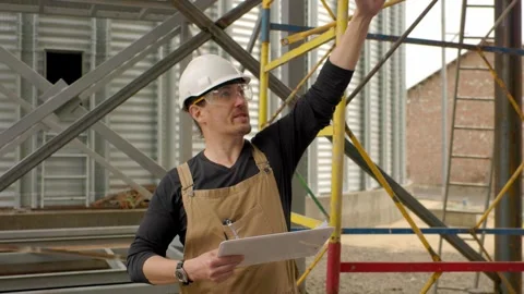 An engineer in a hard hat with a project in hand checks the construction status  Stock Footage 271629550